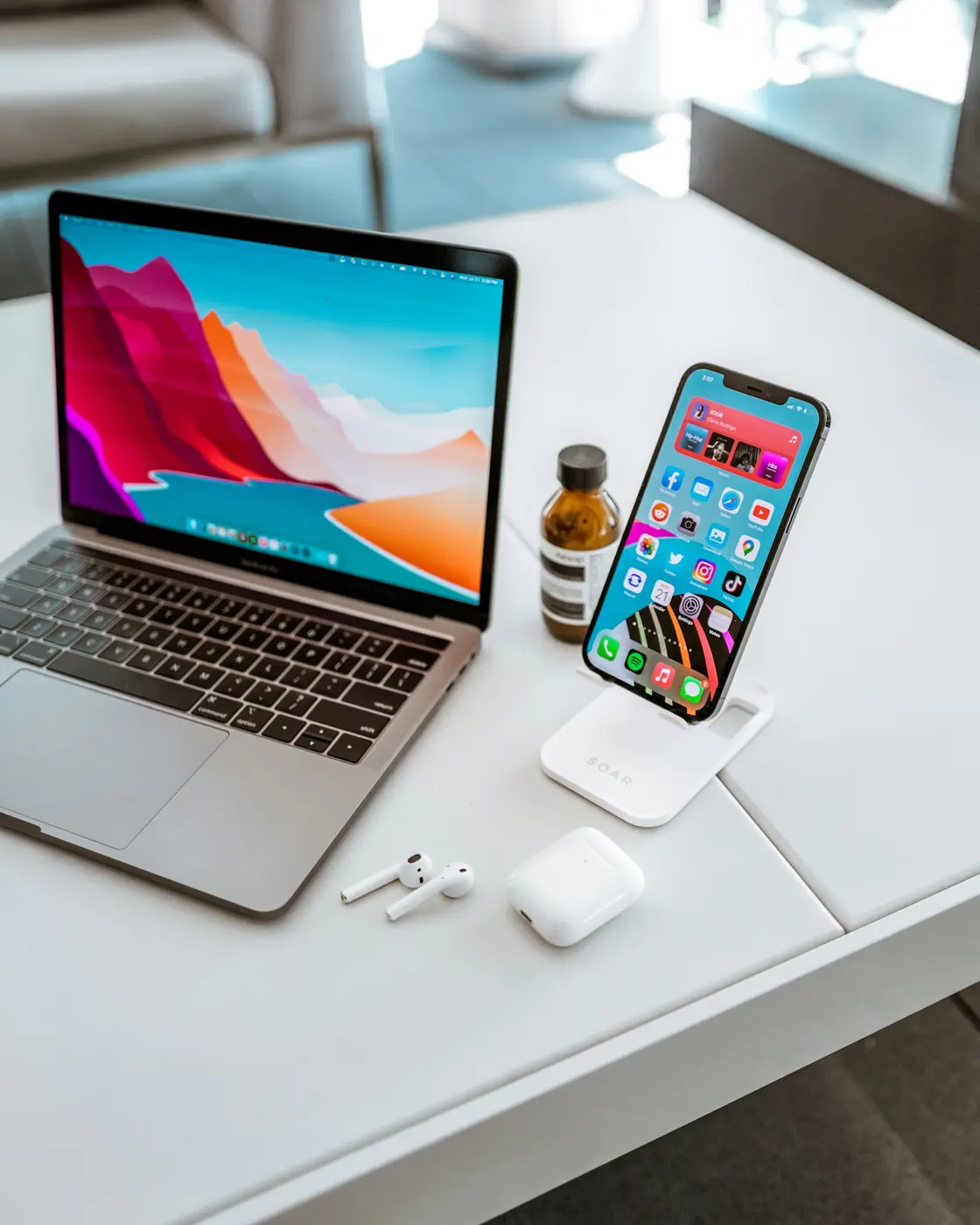A MacBook, iPhone and AirPods on a white desk
